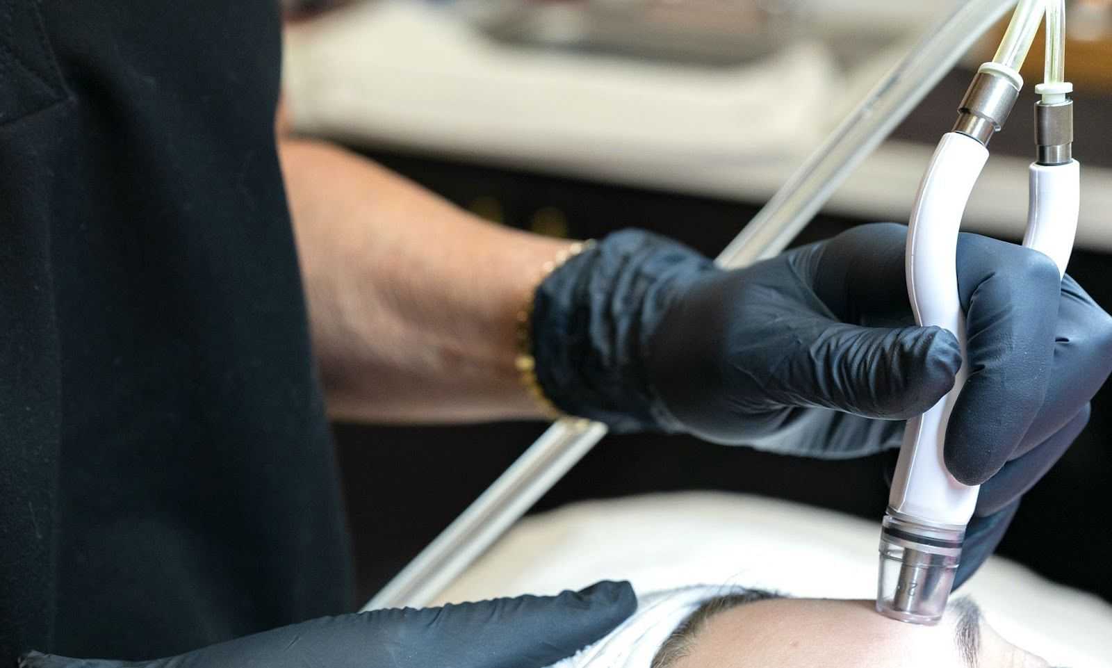 Person performing a facial treatment with specialized equipment in a clinical setting.