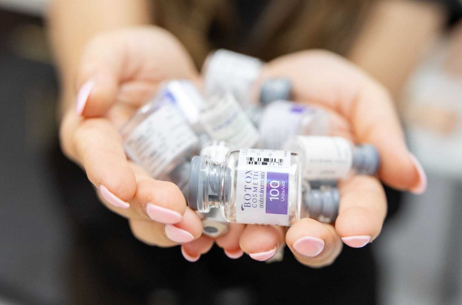 Hands holding multiple small vials with medical labels.