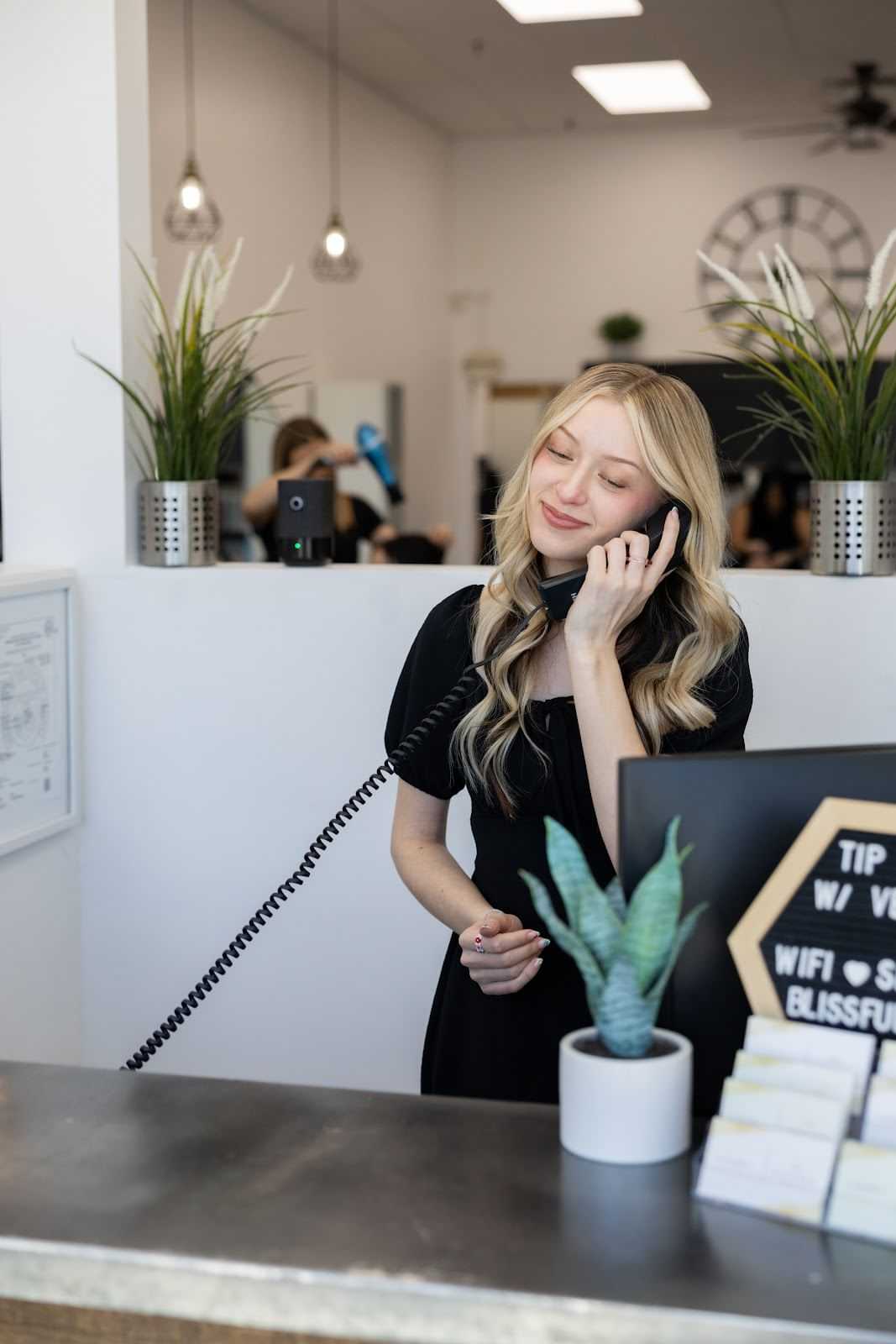Receptionist answering a phone at a modern, plant-decorated front desk.
