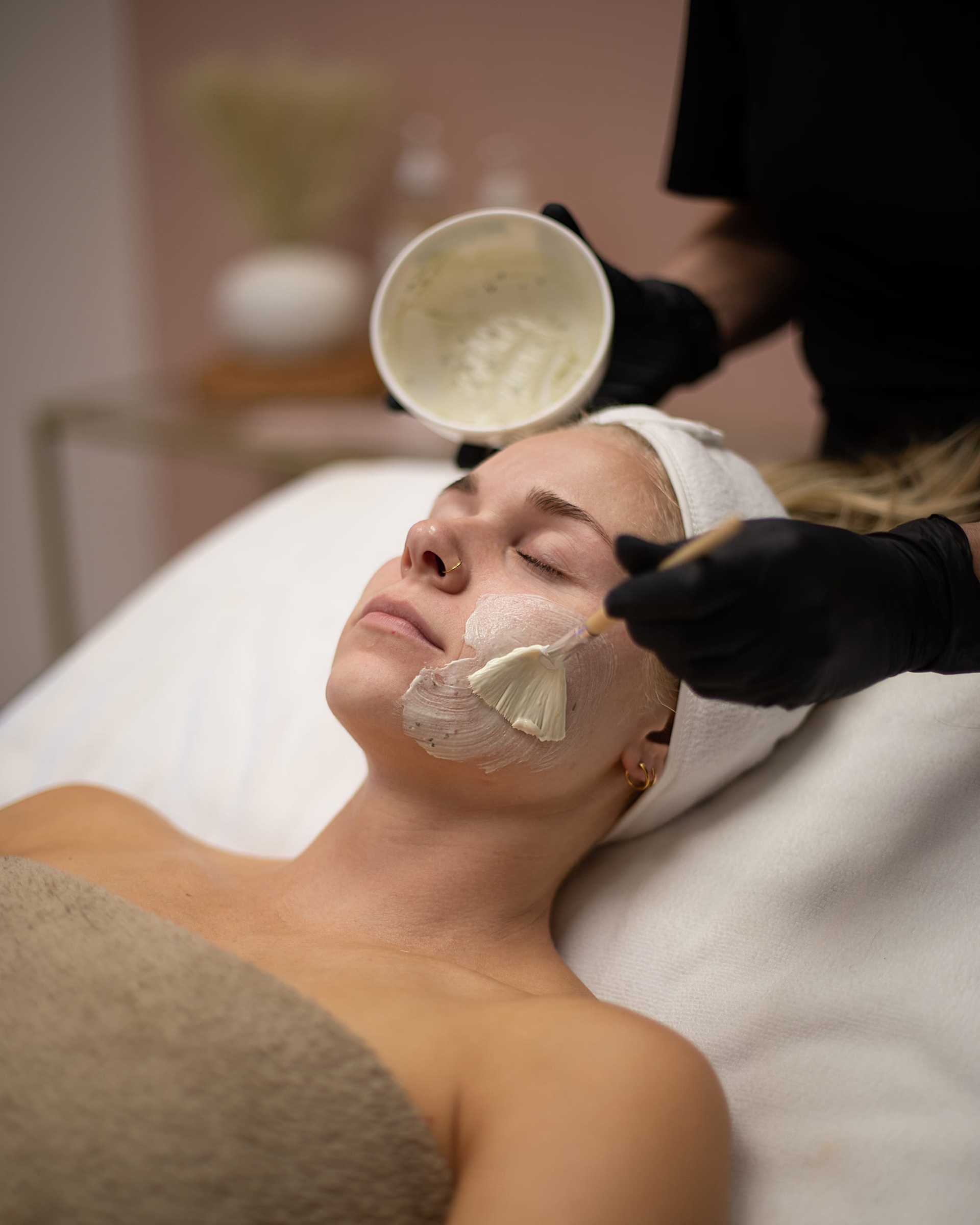 Facial treatment applied to a woman lying on a spa bed by a professional therapist.